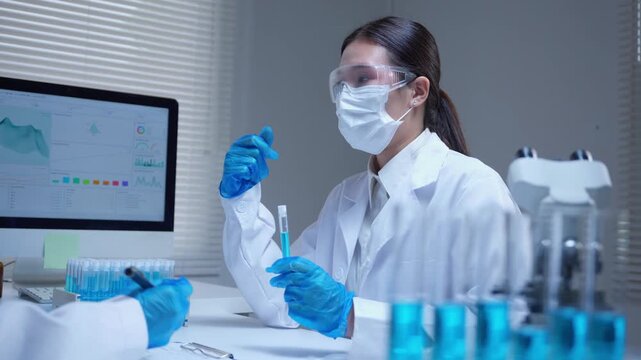 Asian scientist team analyzing test tube samples and discussing data on computer in a modern research laboratory