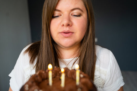 Beautiful woman blowing out three candles on chocolate cake