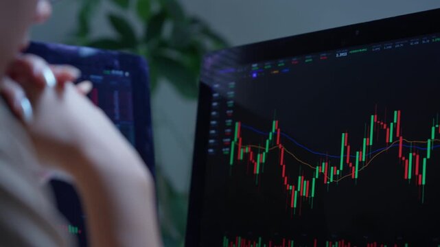 Female trader analyzing cryptocurrency candlestick chart on computer screen at night. Professional investor monitoring stock market data