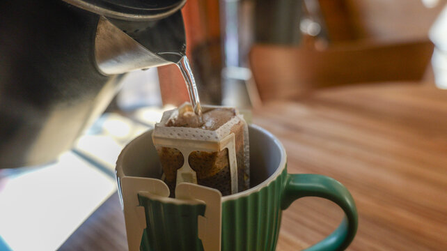 Pouring hot water into a drip coffee bag hanging over a green mug