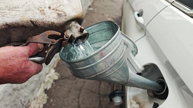 Man refueling car with gasoline using a portable metal canister