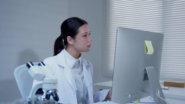 Asian female scientist analyzing blue liquid in test tube and recording data on computer in a modern laboratory research facility