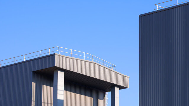 Modern minimal warehouse building exterior with grey corrugated metal wall against clear blue sky. Industrial architecture background with copy space.