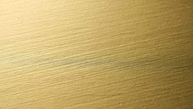 Close up of a brushed gold metallic surface with fine horizontal lines and a warm reflective texture