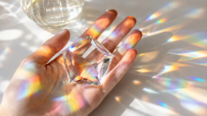 Obraz premium Hand holding glass prism casting rainbow light on surface