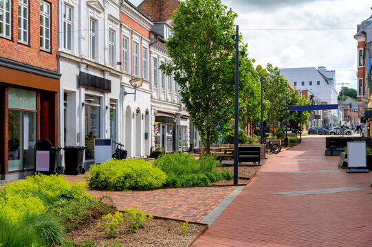 Pedestrian street in Kolding featuring historic buildings, retail shops, landscaped green areas, trees and wide walkways in the modern city center. Denmark