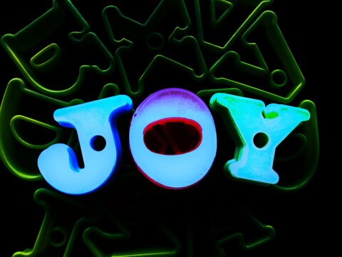 Glowing neon blue word JOY with vivid green alphabet outlines on pitch black background, creative cyberpunk text design
