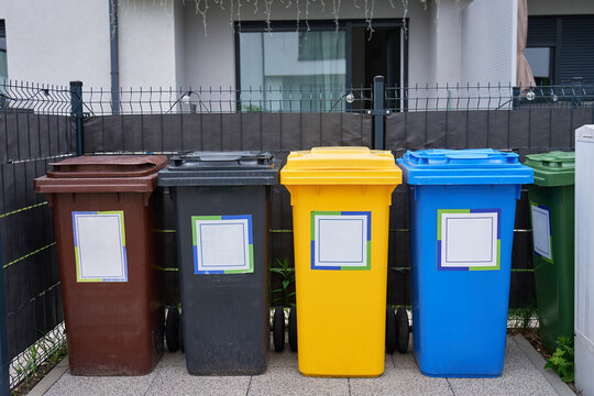 Colored recycling bins stand in front of residential house behind fence
