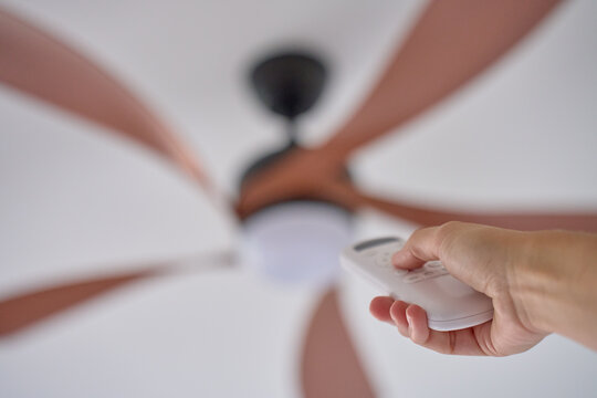 Person using remote control to operate ceiling fan mounted on white ceiling