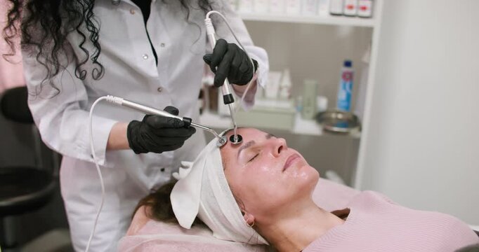 Cosmetician working. Aesthetic therapy. Female in black gloves using professional device for modern facial microcurrent procedure.