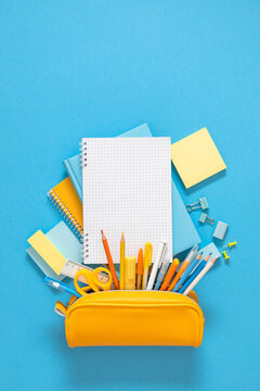Yellow pencil case with school stationery under open blank notebook on blue background. Vertical back to school banner template with copy space, education concept layout, student desk flat lay.