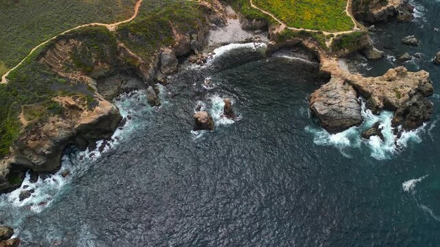 Aerial drone footage of the dramatic coastline at Point Lobos in Big Sur, California. The shot captures rugged cliffs, turquoise Pacific Ocean waves, rocky coves, and untouched natural landscapes.