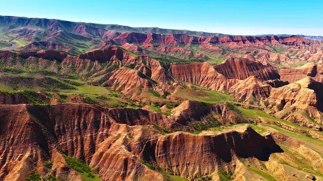 Aerial view of striking red sandstone cliffs and green valleys in Xinjiang, China.