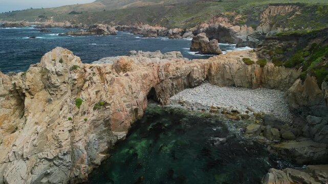 Aerial drone footage of the dramatic coastline at Point Lobos in Big Sur, California. The shot captures rugged cliffs, turquoise Pacific Ocean waves, rocky coves, and untouched natural landscapes.