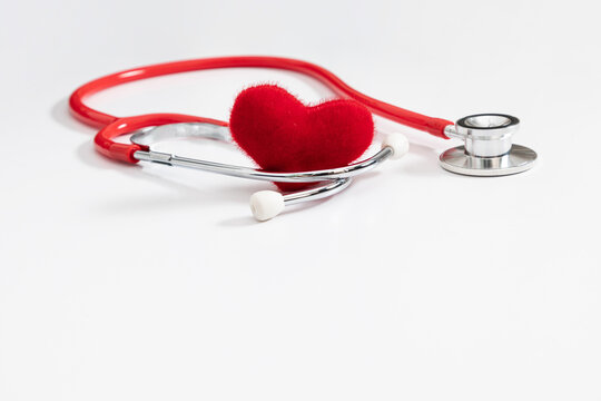 Red medical stethoscope with soft plush heart on white surface. Healthcare template with copy space, cardiology checkup concept, insurance background, doctor cardiovascular exam, life safety banner. 