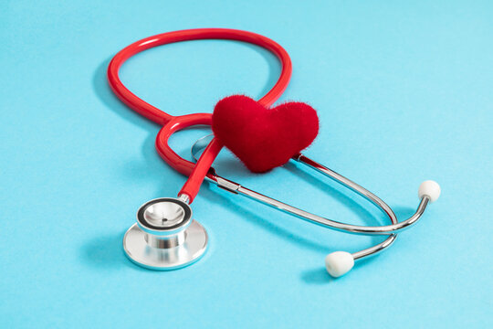 Red stethoscope and plush decorative heart on bright blue background. Medical concept of cardiology health care, professional heart checkup, insurance protection, life saving, hospital exam.