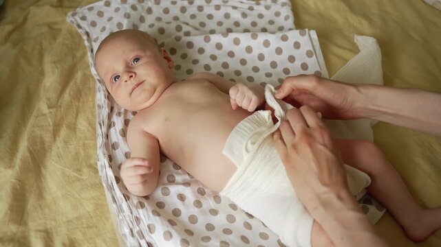 Top down view of a mother's hands carefully changing her infant's eco friendly reusable cloth diaper, promoting sustainable parenting and gentle childcare in a cozy home environment