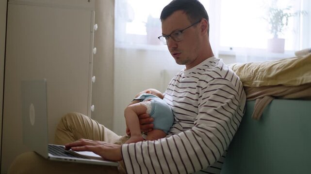 Multitasking father attempting to work remotely on a laptop while caring for his sleeping newborn baby, highlighting the challenges and realities of modern parenthood and work life balance