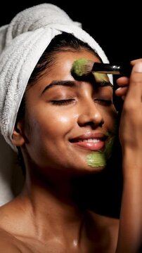 Young Woman Applying Green Face Mask with Brush, Enjoying Skincare Routine.