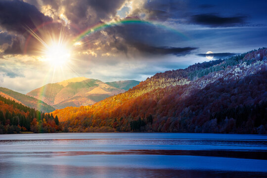 landscape with lake in autumn. day meet night. sun and moon over scenic view of forest reflection on the lake surface at twilight. rika river water reserve. transcarpathia in fall season