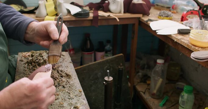 Shoemaker workshop. Handmade footwear. Unrecognizable craftsman hands smearing sole using glue with brush in professional factory.