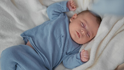Baby boy sleeping with clenched fist and closed eyes in knit blue onesie on soft white blanket in studio  gentle soothing serenity. © Krakenimages.com