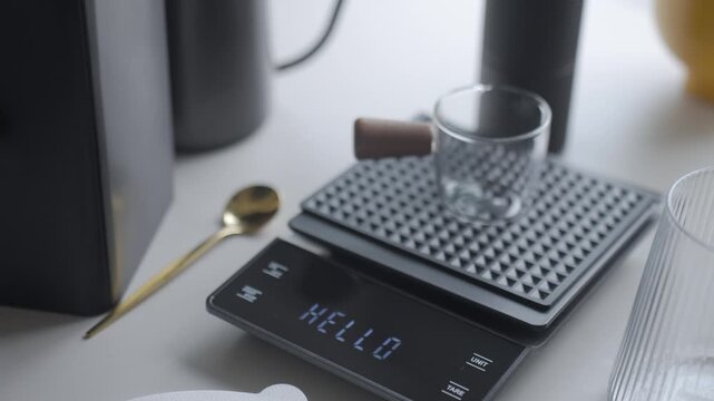Woman placing glass cup on digital scale and turning it on during coffee setup. Concept of manual coffee brewing and drink preparation