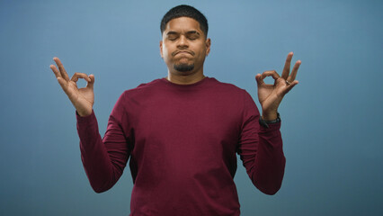 Fototapeta premium Man with hands pressed together praying in studio, eyes closed and wearing maroon sweater; calm reflection.