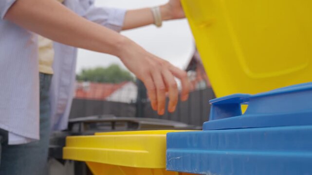 Woman places plastic bottle into yellow recycling bin for recycling collection. Concept of plastic waste sorting and household recycling