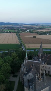 Vertical video of flyover side of Marienburg Castle towers with fields beyond