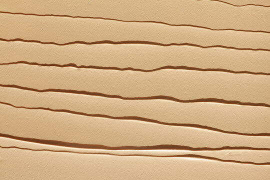 Beige liquid foundation cream texture background. Smooth cosmetic concealer smudge backdrop with brush stroke lines. Makeup face tone paste close up view. Beautiful nude skin care or beauty concept.
