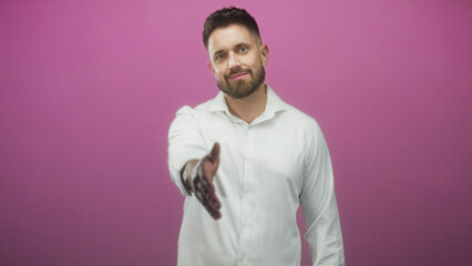 Man with beard and white shirt extends right hand offering handshake in studio against pink wall  friendly welcome trust connection. © Krakenimages.com