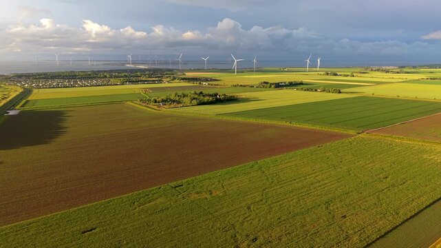 Aerial wide angle perspective of beautiful agricultural patchwork fields and a large wind turbine farm on the distant coastal horizon under a dramatic summer sky