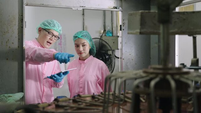 Professional Asian maintenance engineer and technician in food and beverage drink factory in uniform with tablet while talking and discussing machine operation in production line at industry facility.