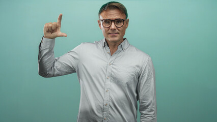 Naklejka premium Man in studio holds thumb and index finger showing a small gap while looking sideways, wearing glasses and a collared button shirt; thoughtful reflection.