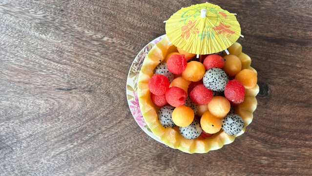 Fresh tropical fruit bowl in carved melon with watermelon, cantaloupe and dragon fruit on wooden table top view