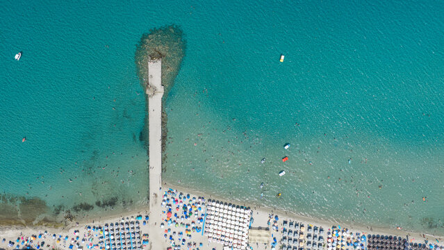 Pier Extending into Turquoise Waters by Crowded Greek Beach