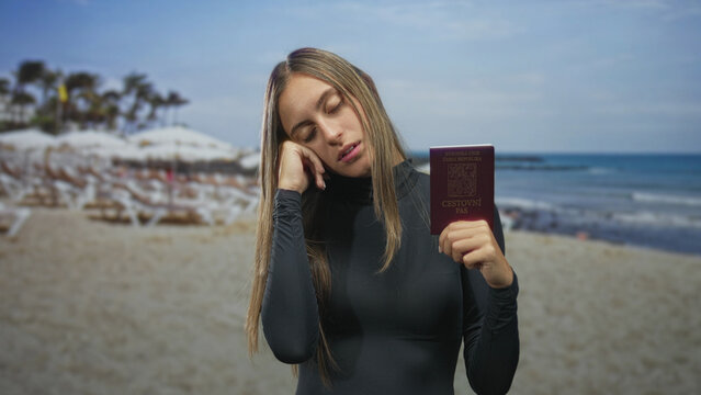Woman holding passport, head resting on hand, eyes closed and slouched posture at sunny beach with umbrellas and sea in view; tired rest.