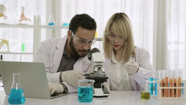 Two professional scientists and researchers are excited and happy about their success in conducting chemistry experiments on a medical vaccine, using a microscope and laptop in the science laboratory.