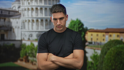 Fototapeta premium Man with arms crossed and head down by a building at the pisa tower outdoor plaza, contemplating the scene; pensiveness reflection.
