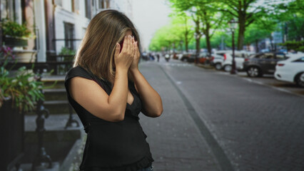 Fototapeta premium Woman covers mouth with hands and wears glasses while standing on a tree lined street near parked cars; surprise privacy vulnerability.