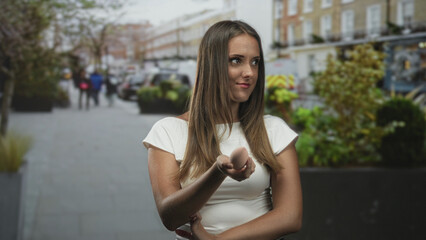 Fototapeta premium Woman holds makeup sponge between fingers smiling and offering it with palm up on street; confidence.