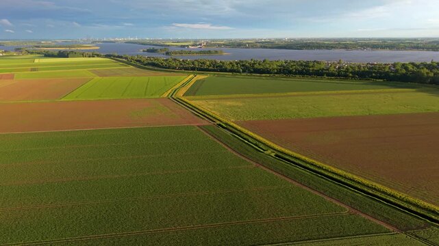 Aerial wide angle panoramic view of vast geometric agricultural patchwork fields next to a large scenic river and lush green banks under a dramatic evening summer sky