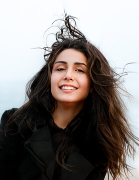 Portrait de jeune femme souriante aux longs cheveux bruns balay&eacute;s par le vent