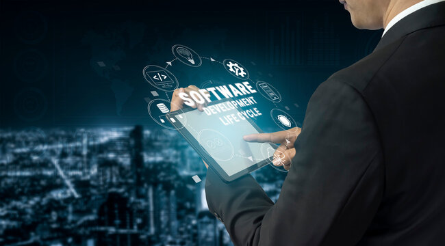 Conceptual Image of Businessman Using Tablet to Illustrate Software Development Lifecycle with Cityscape Background at Night Quark.