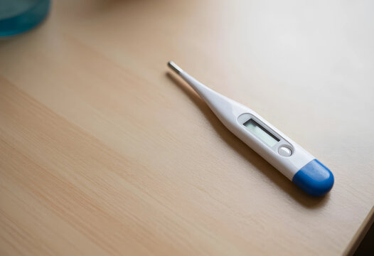 Digital medical thermometer with a blank screen on a light wooden table, health care and illness