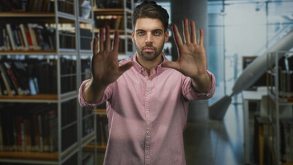 Hispanic man with beard holds both palms up toward camera while standing among bookshelves in building  concentration privacy. © Krakenimages.com