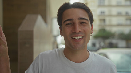 Man smiling with face forward, left hand on doorway, wearing white tshirt and hoop earring on street near building entrance  casual warmth. © Krakenimages.com