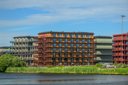 Colorful waterfront apartment blocks beside reeds and calm water.