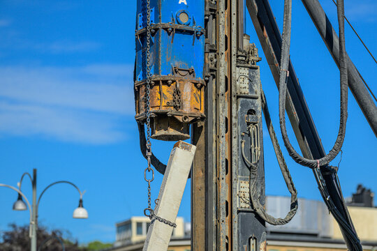Industrial pile driving machinery gripping concrete beam on urban site.